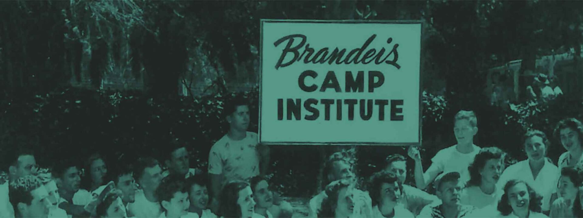 The image features a group of adults in front of a sign that reads "Brandeis Camp Institute," surrounded by greenery, conveying a communal, possibly historical setting.