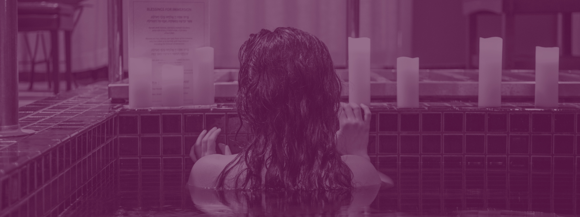 A person relaxes in a tiled pool surrounded by lit candles, creating a peaceful atmosphere. The setting looks calm and serene.